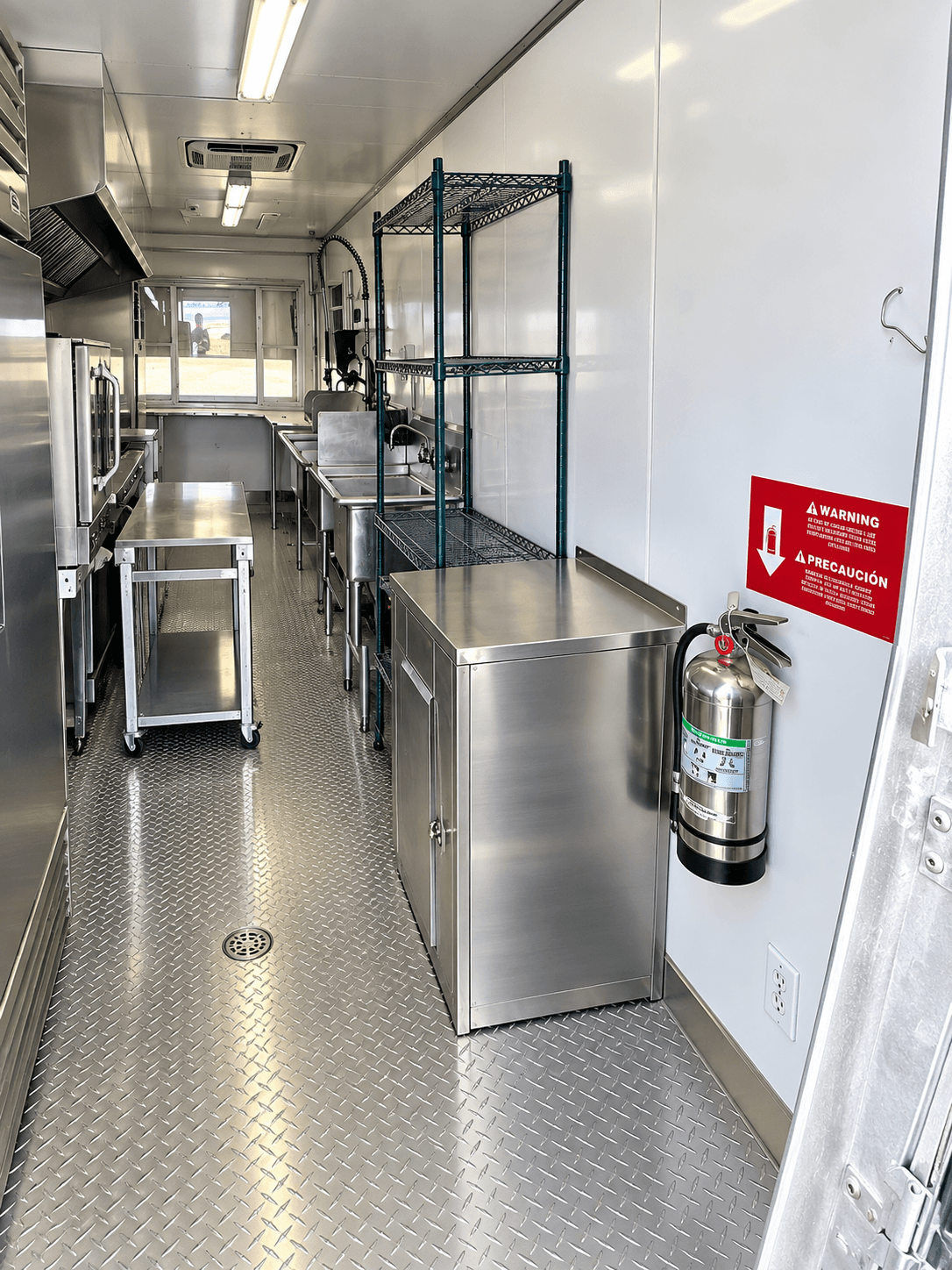 Interior of a commercial mobile kitchen trailer showcasing stainless steel cooking, preparation, and washing equipment